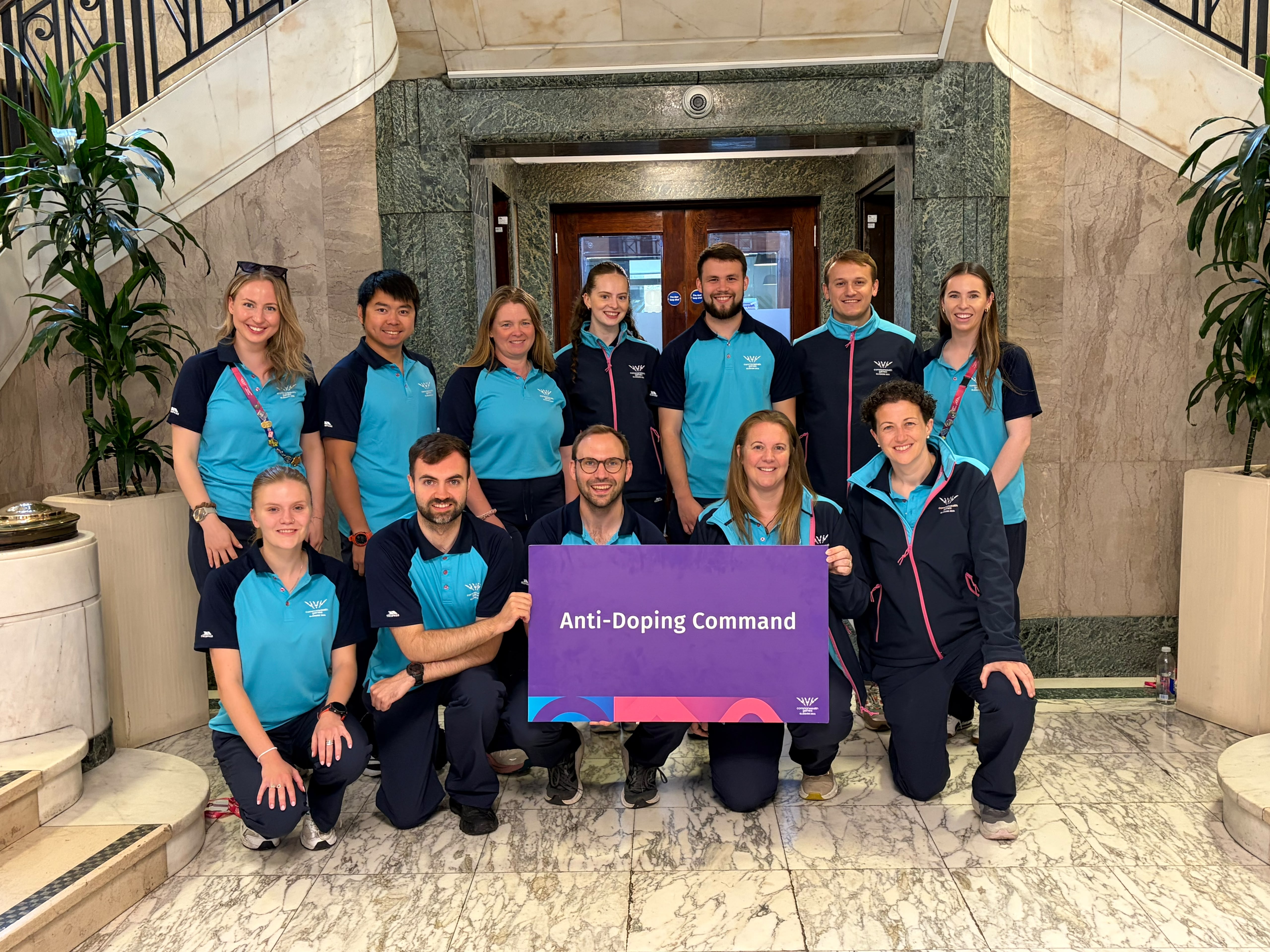 12 members of the Anti-Doping Command pose for a photo inside a hotel foyer.